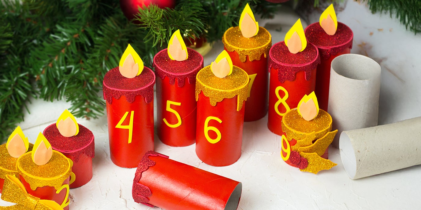 Bastelideen für Weihnachten: Adventskalender aus bemalten Klopapierrollen in Kerzenform mit gelben Zahlen und Flammen vor Tannenzweigen