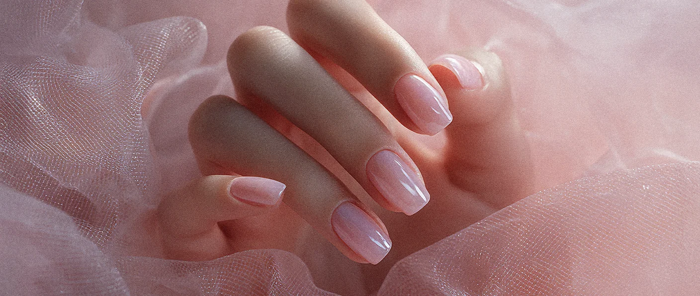 Nahaufnahme einer eleganten Frauenhand mit einer milchig-rosa Maniküre, die sanft auf einem zarten, rosafarbenen Tüllstoff ruht